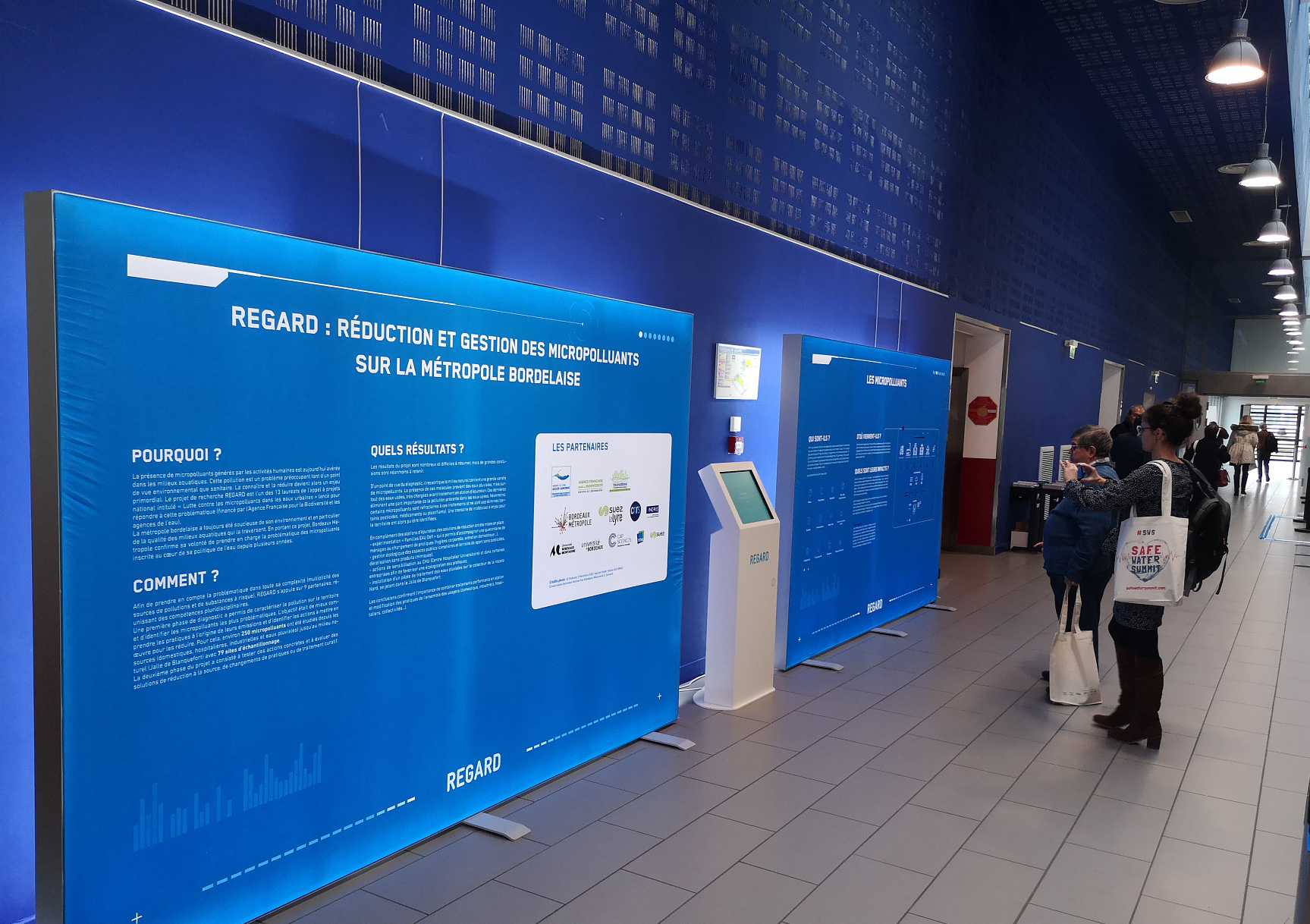Personnes dans un hall regardant une exposition sur l'étude "REGARD" de la station d'épuration des eaux usées de Masseret.